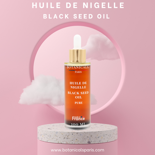 Une bouteille de 100ml d'huile de nigelle bio devant un fond rose, parsemé de léger nuage